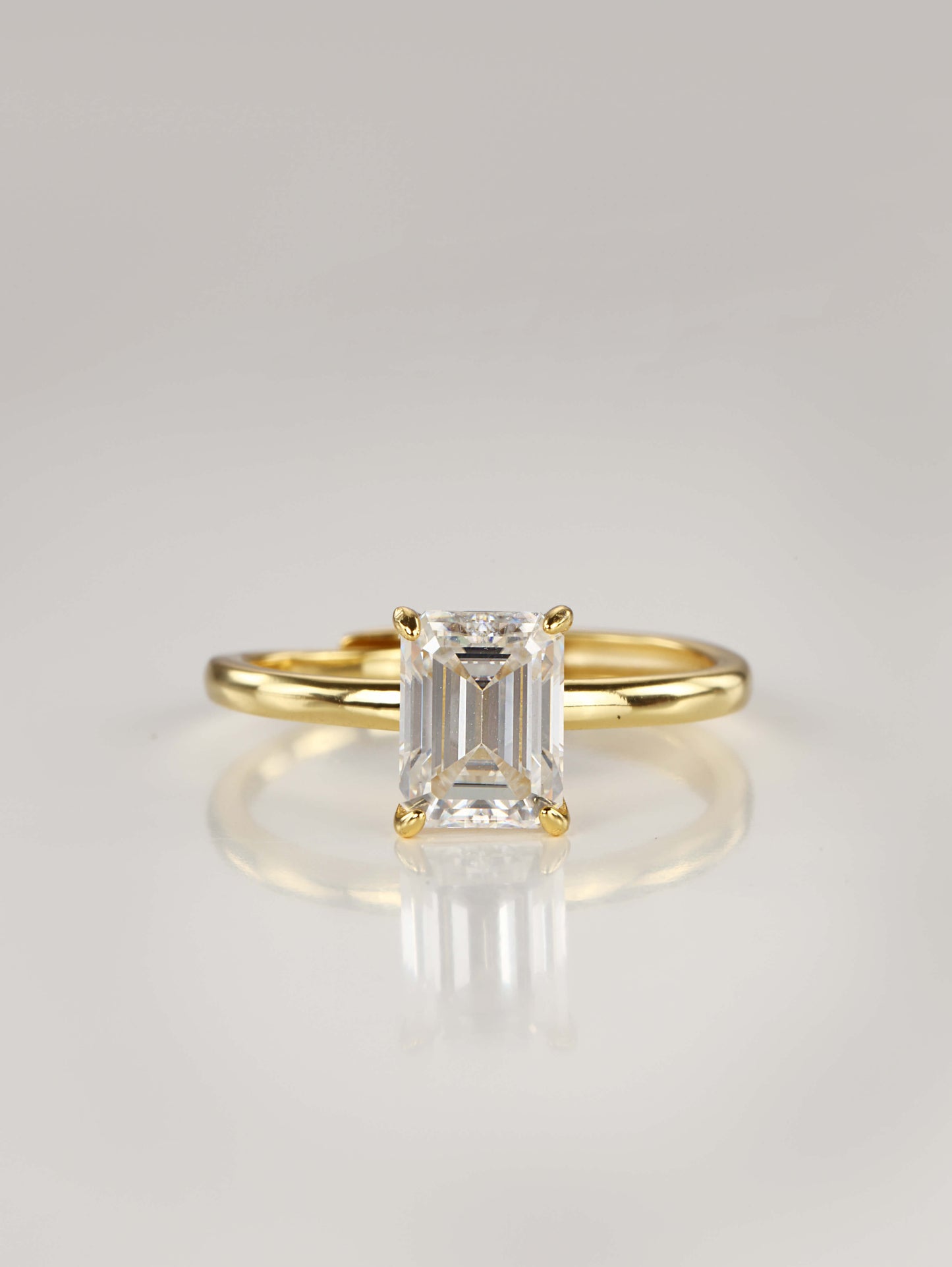 A gold adjustable ring featuring a 2-carat emerald-cut moissanite centre stone in a 4-prong setting, resting on a clean white background