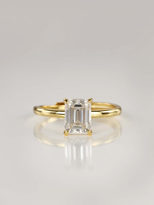 A gold adjustable ring featuring a 2-carat emerald-cut moissanite centre stone in a 4-prong setting, resting on a clean white background