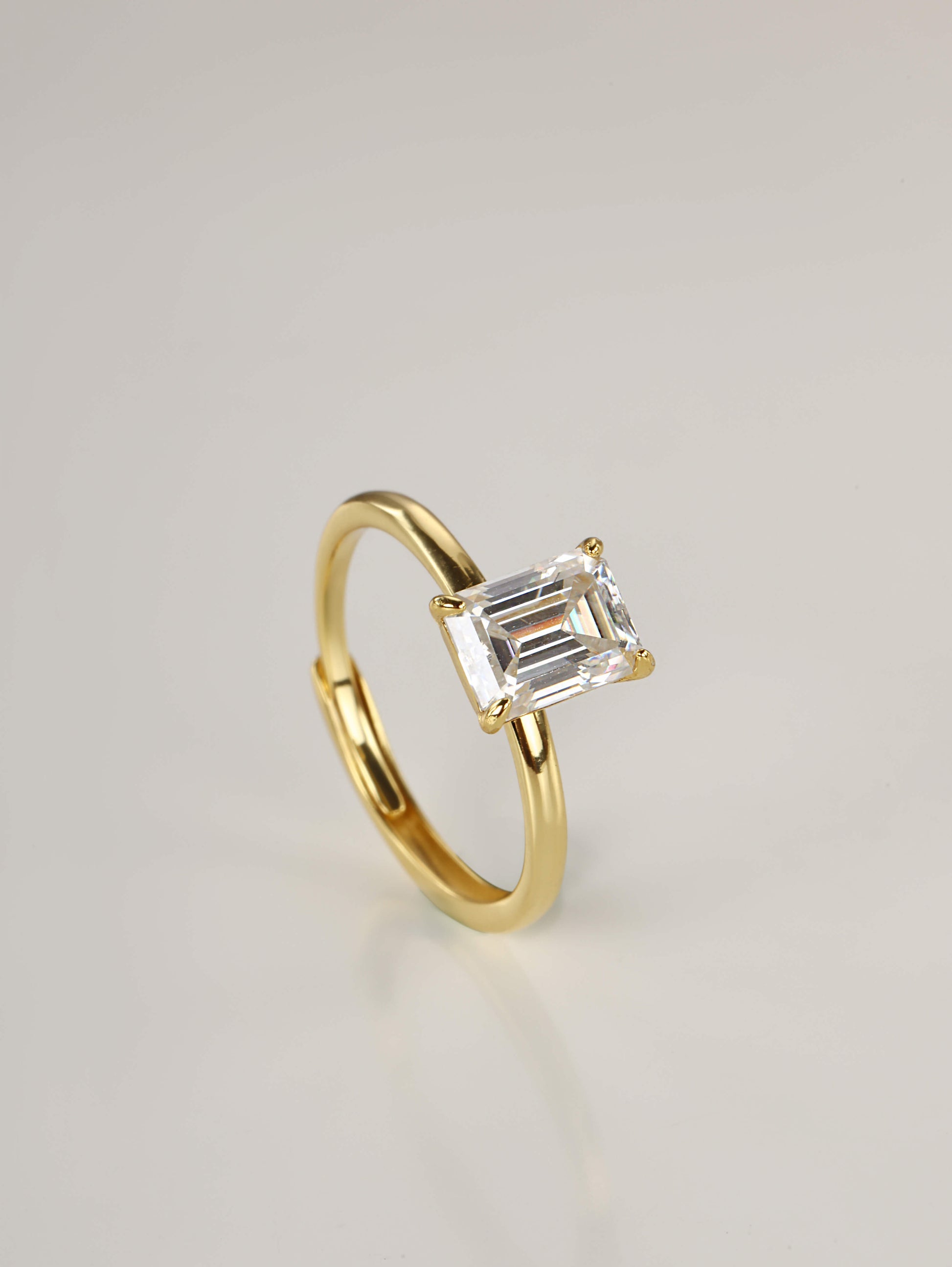 A close-up of a hand wearing a stunning 2-carat emerald cut moissanite solitaire ring in yellow gold, showcasing the clear step-cut facets in natural lighting.