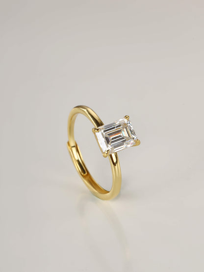 A close-up of a hand wearing a stunning 2-carat emerald cut moissanite solitaire ring in yellow gold, showcasing the clear step-cut facets in natural lighting.