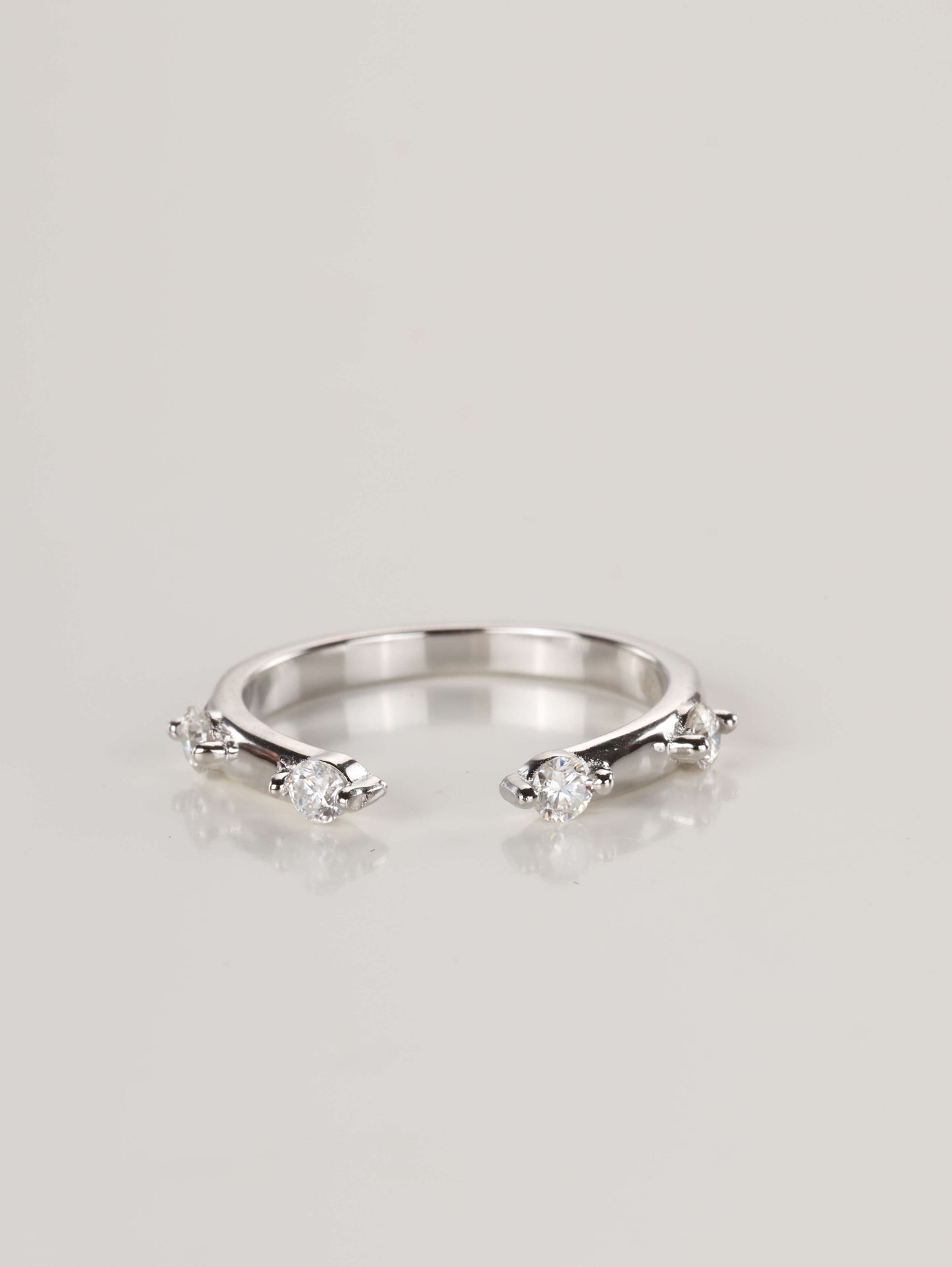 Close-up of a delicate 925 silver open front ring resting on a pale surface, featuring four spaced moissanite stones totalling 0.24ct.