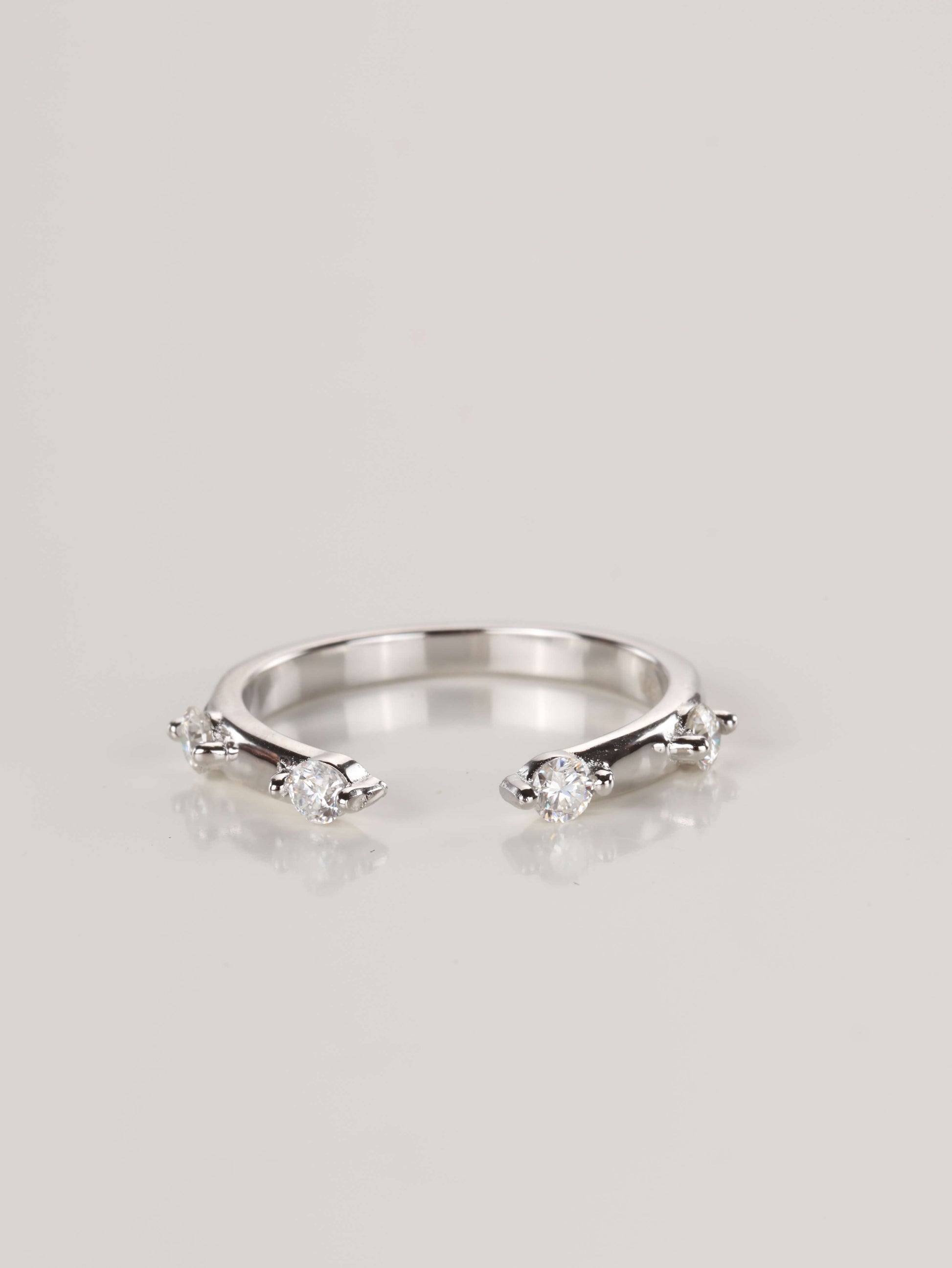 Close-up of a delicate 925 silver open front ring resting on a pale surface, featuring four spaced moissanite stones totalling 0.24ct.