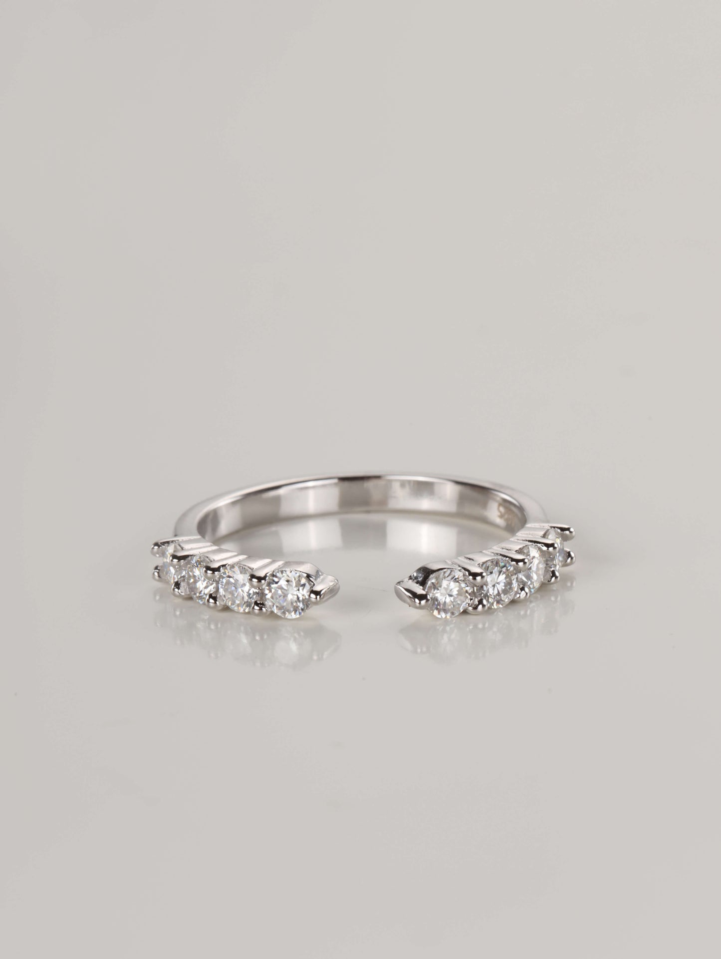 Close-up of a silver open front eternity ring resting on a pale surface, featuring a gap in the centre and 0.48ct of brilliant moissanite stones along the top band.