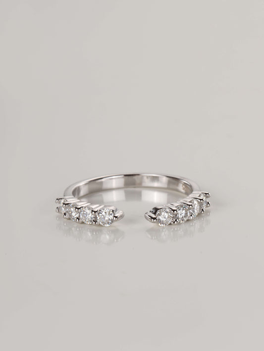 Close-up of a silver open front eternity ring resting on a pale surface, featuring a gap in the centre and 0.48ct of brilliant moissanite stones along the top band.