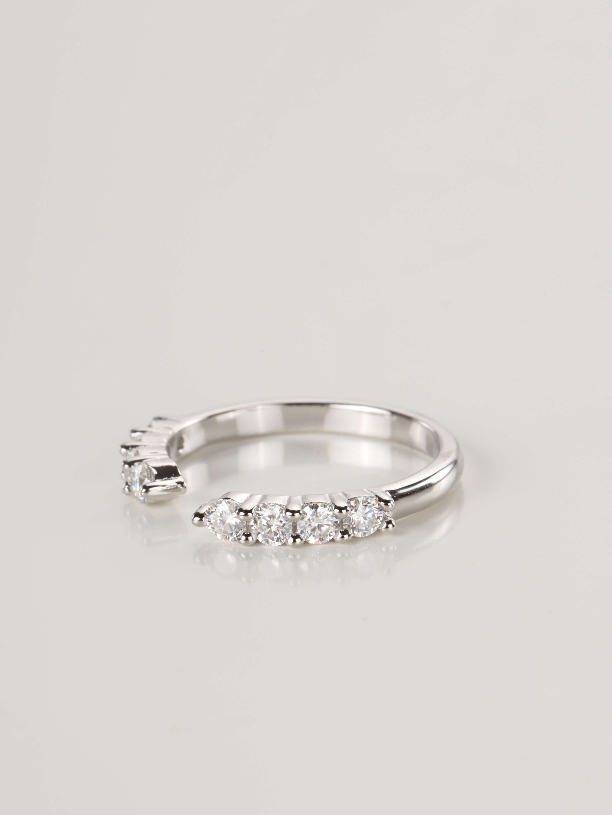 A woman's hand wearing a silver 0.48ct open cuff eternity ring, showing how the gap design perfectly frames the base of an engagement ring.