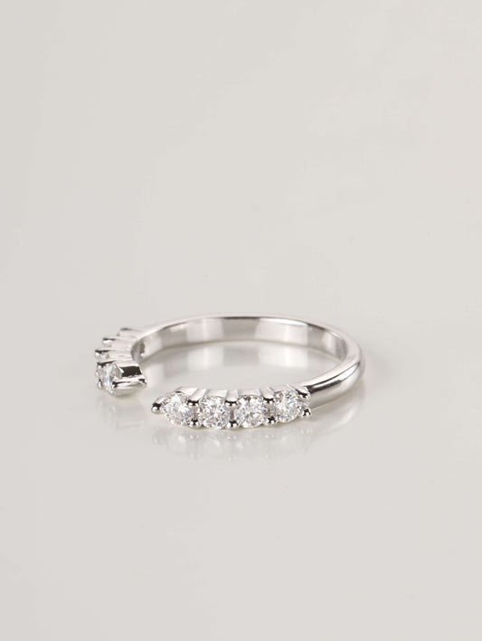 A woman's hand wearing a silver 0.48ct open cuff eternity ring, showing how the gap design perfectly frames the base of an engagement ring.