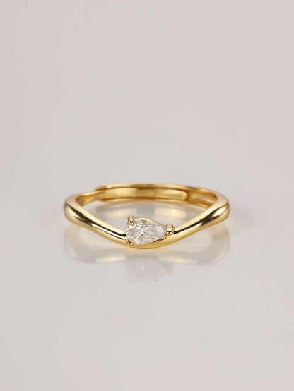 Close-up of a gold adjustable ring featuring a wavy band and a horizontally set 0.5ct pear-cut moissanite, resting on a pale surface.