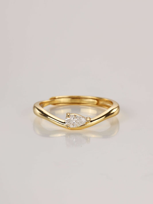 Close-up of a gold adjustable ring featuring a wavy band and a horizontally set 0.5ct pear-cut moissanite, resting on a pale surface.