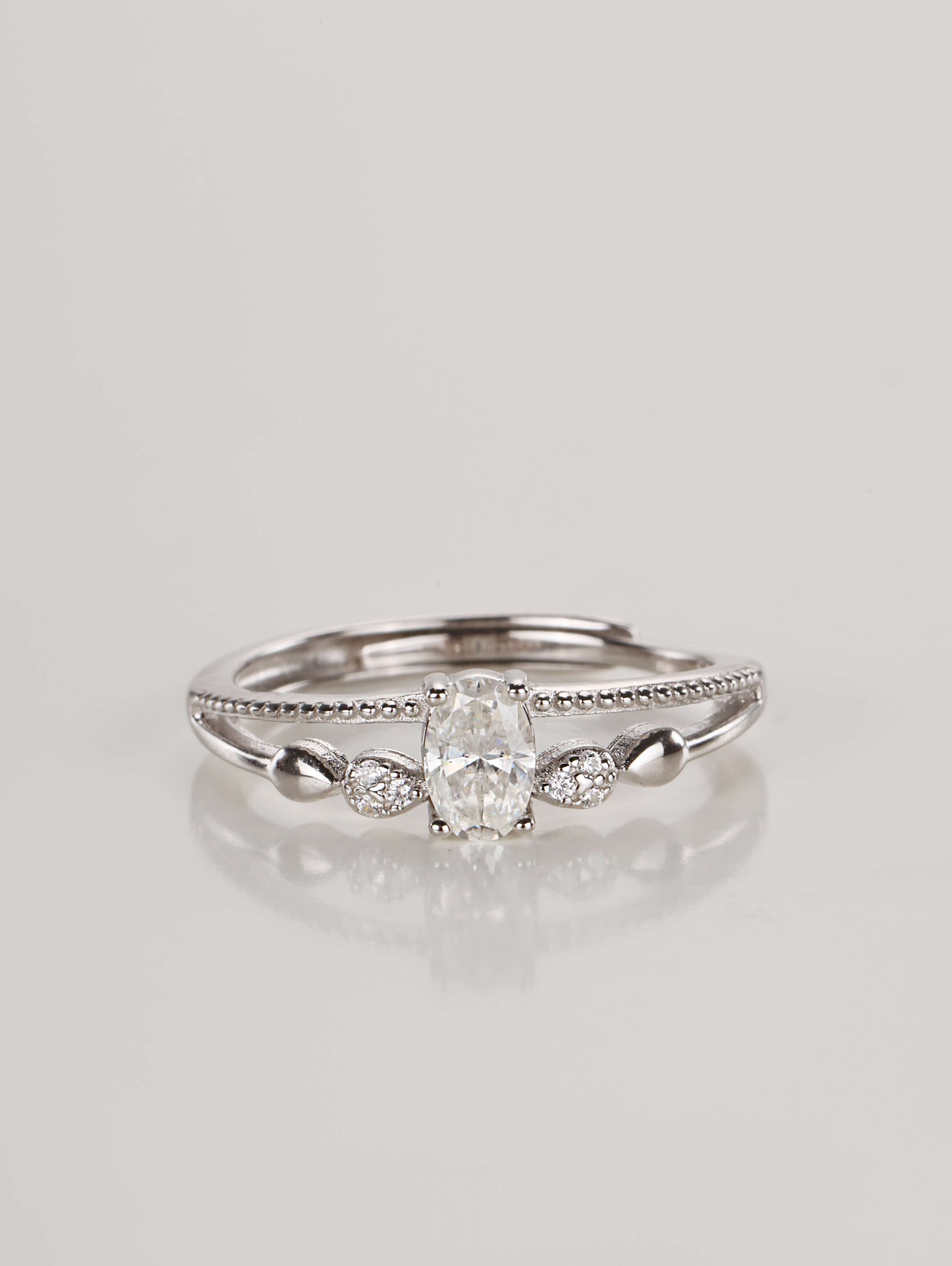 A silver adjustable ring featuring a 0.5-carat oval moissanite centre stone and a double-layer band with beaded detailing, resting against a clean white background