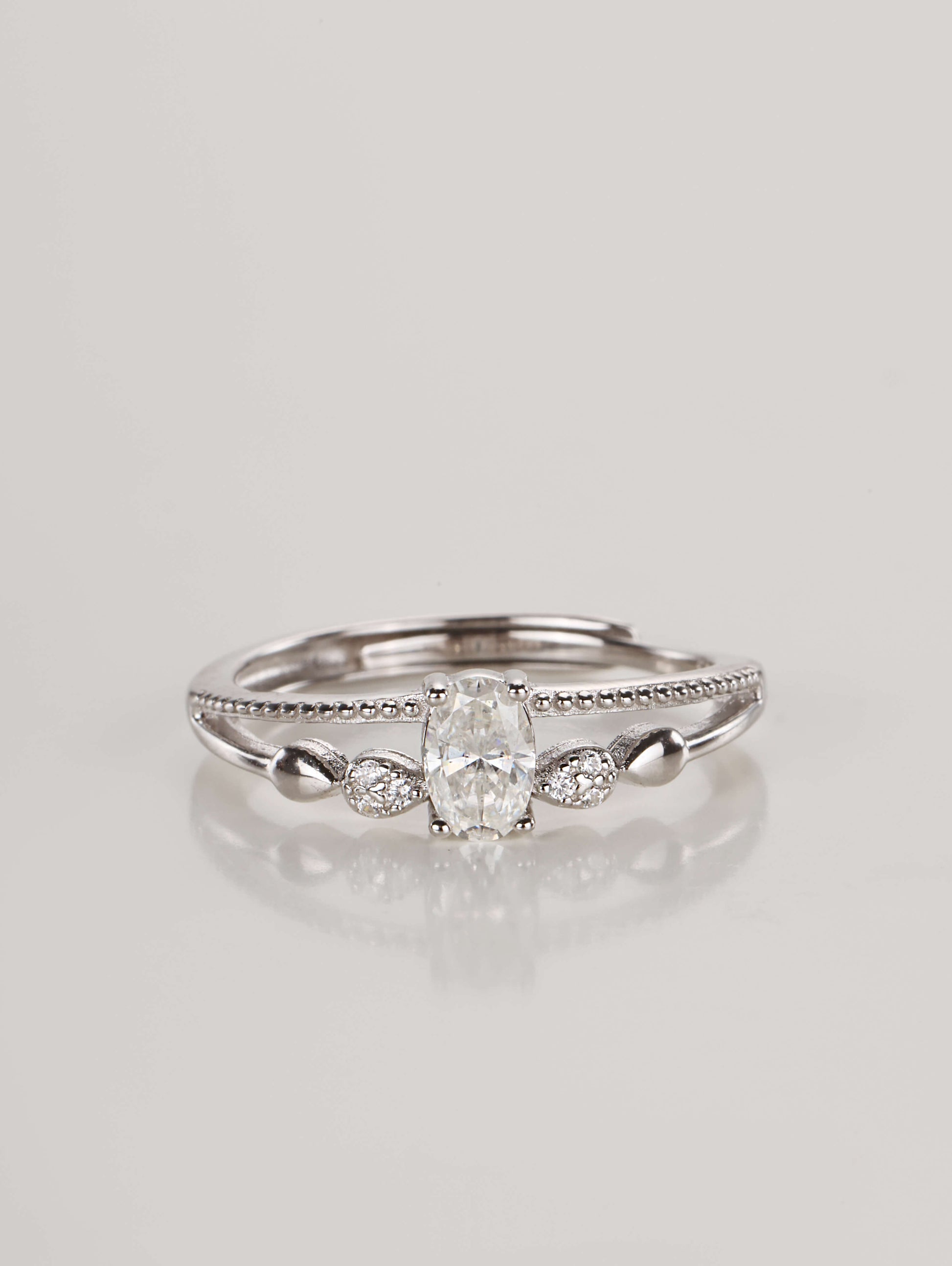 A silver adjustable ring featuring a 0.5-carat oval moissanite centre stone and a double-layer band with beaded detailing, resting against a clean white background