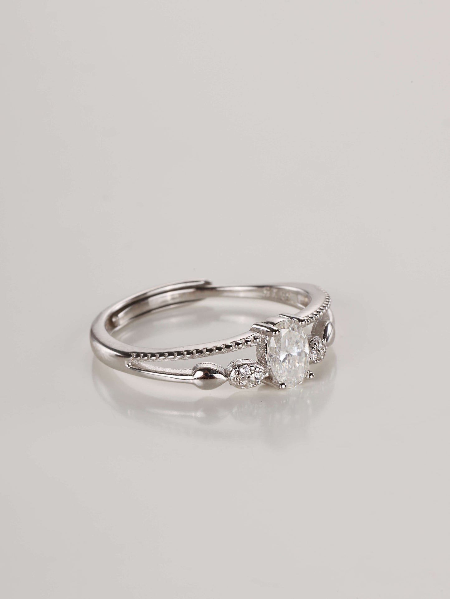 Close-up macro shot of the 925 sterling silver ring highlighting the split-shank double band, delicate milgrain texture, and brilliant oval moissanite stone.
