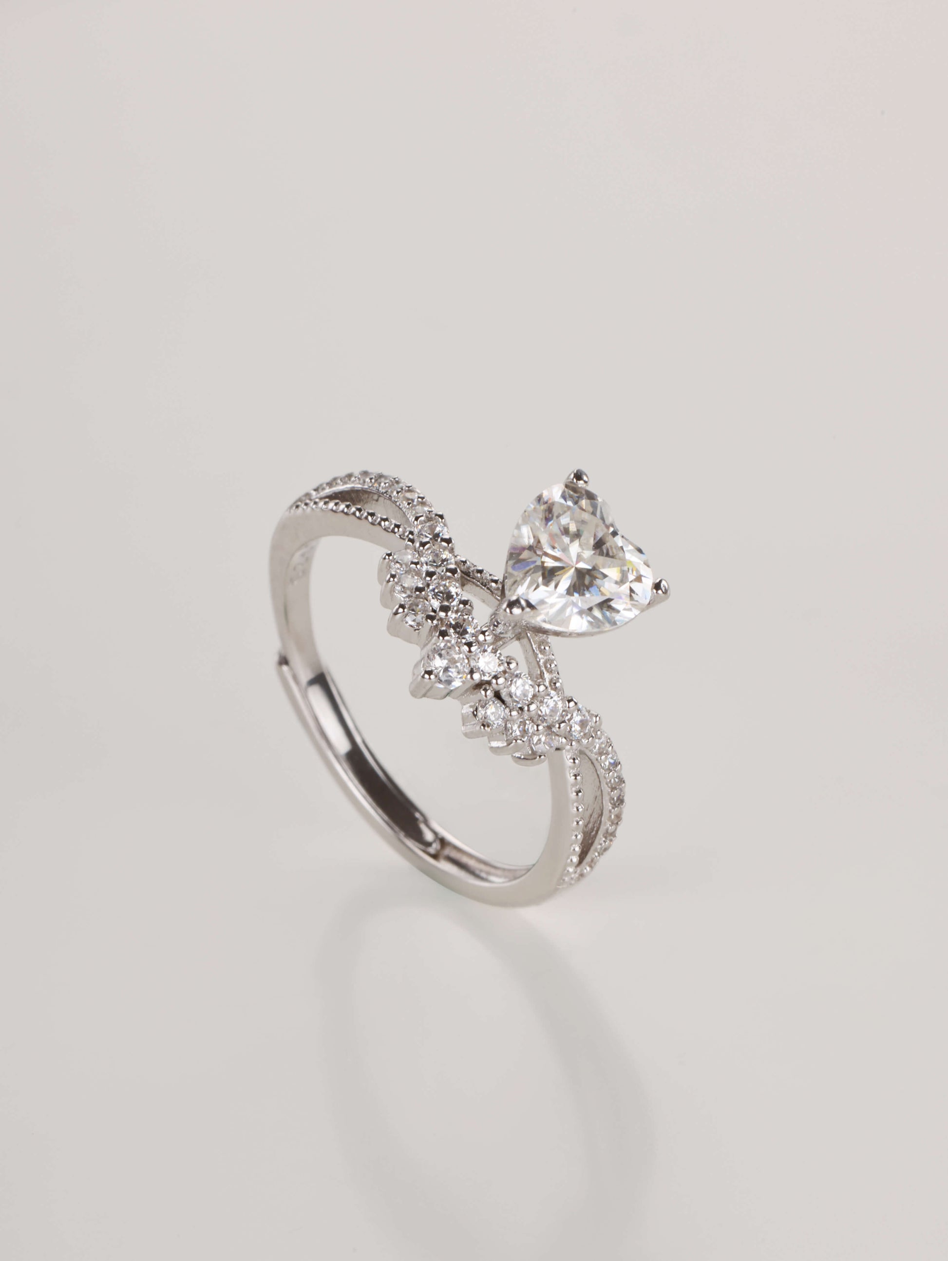 Side angle view of an adjustable sterling silver heart ring showing the prong setting and side gems