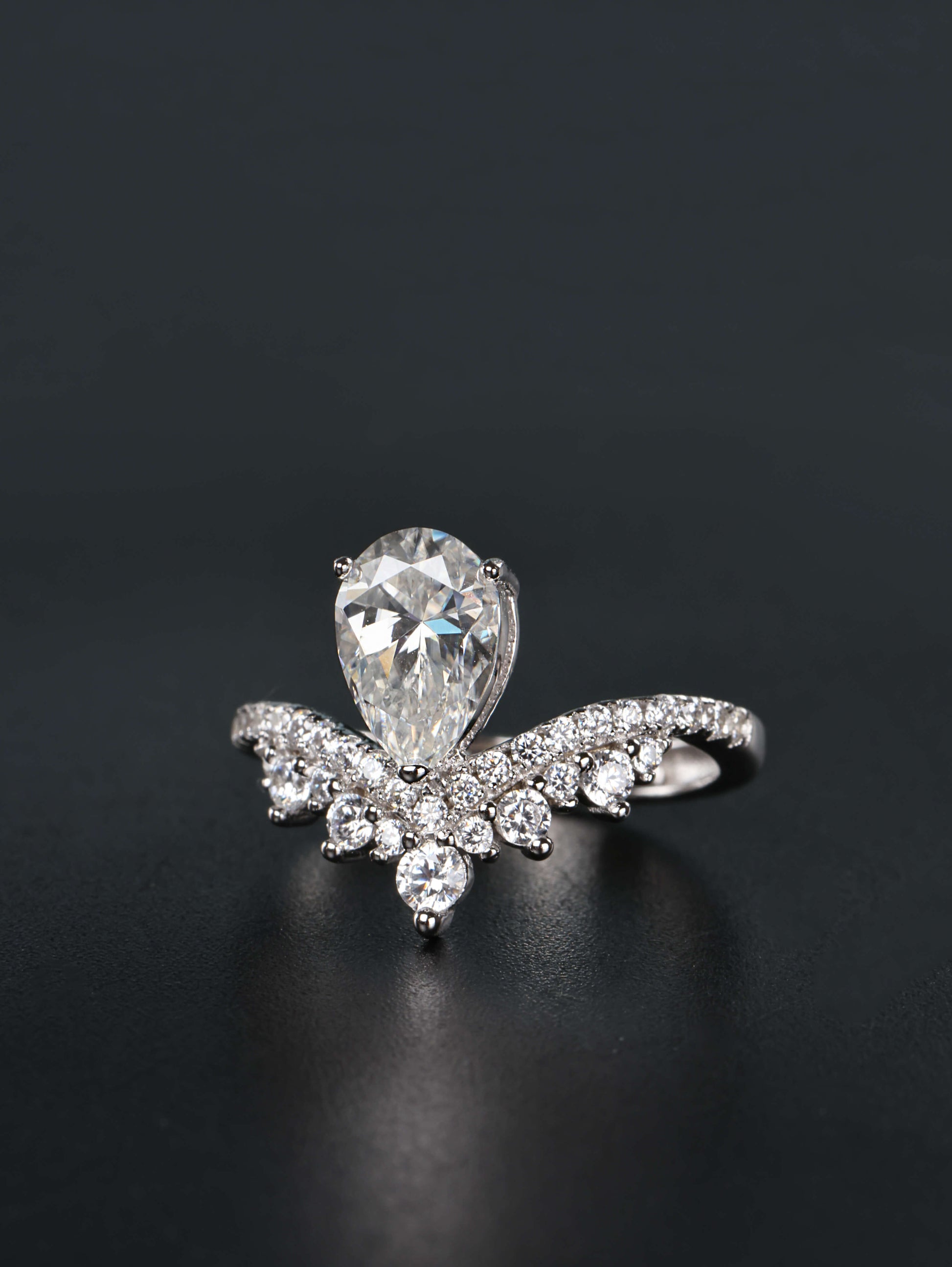 Alternative pear shaped moissanite engagement ring with a chevron tiara crown worn on a finger