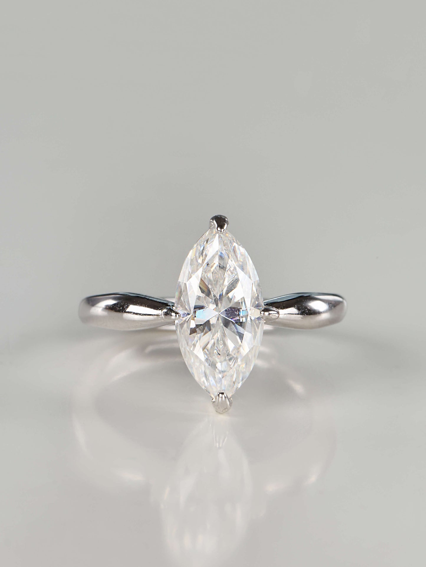 Close up of a brilliant marquise cut moissanite solitaire ring set in 925 sterling silver, featuring a tapered polished band and secure V-prongs, resting on a clean white background.