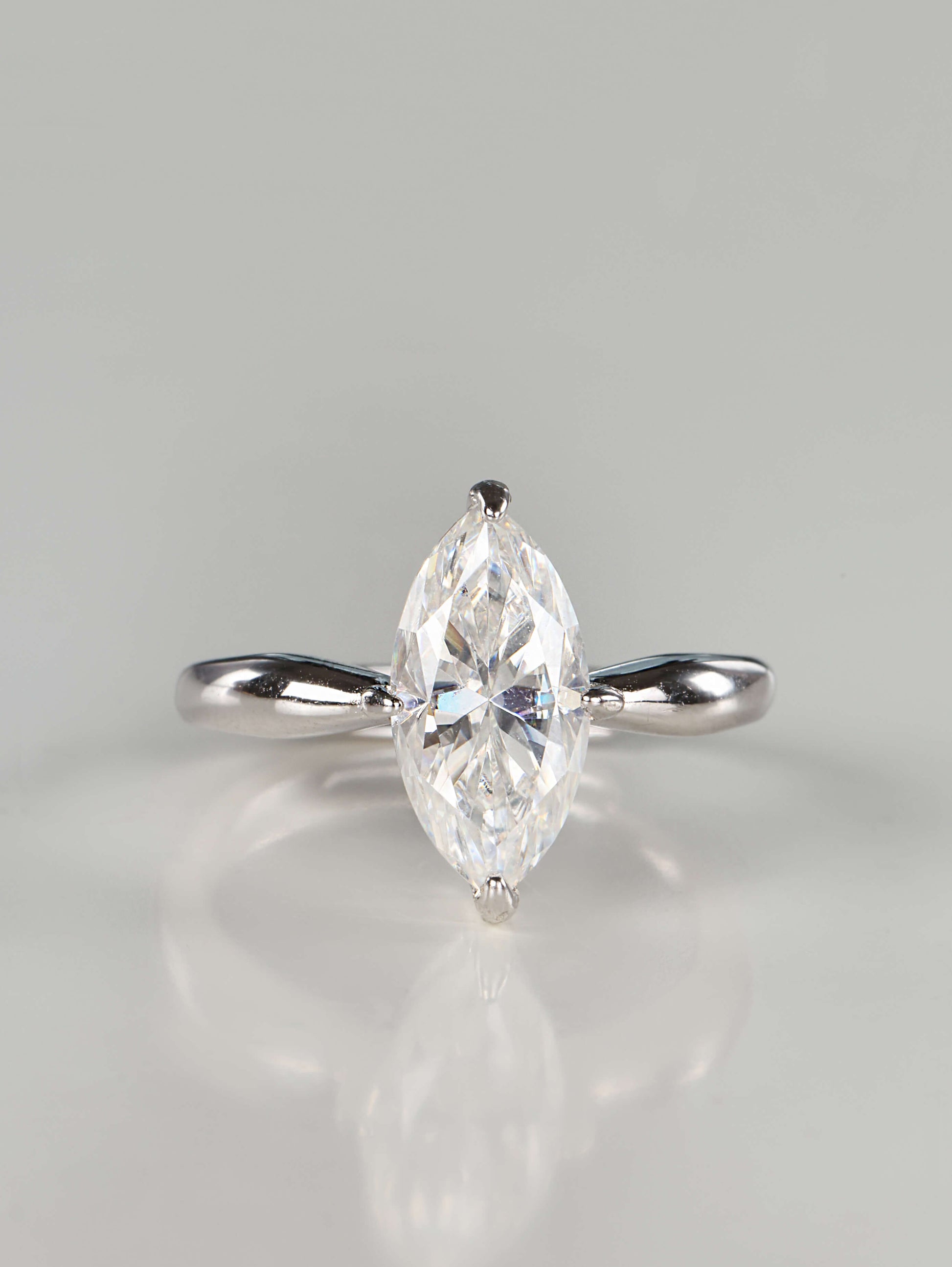 Close up of a brilliant marquise cut moissanite solitaire ring set in 925 sterling silver, featuring a tapered polished band and secure V-prongs, resting on a clean white background.