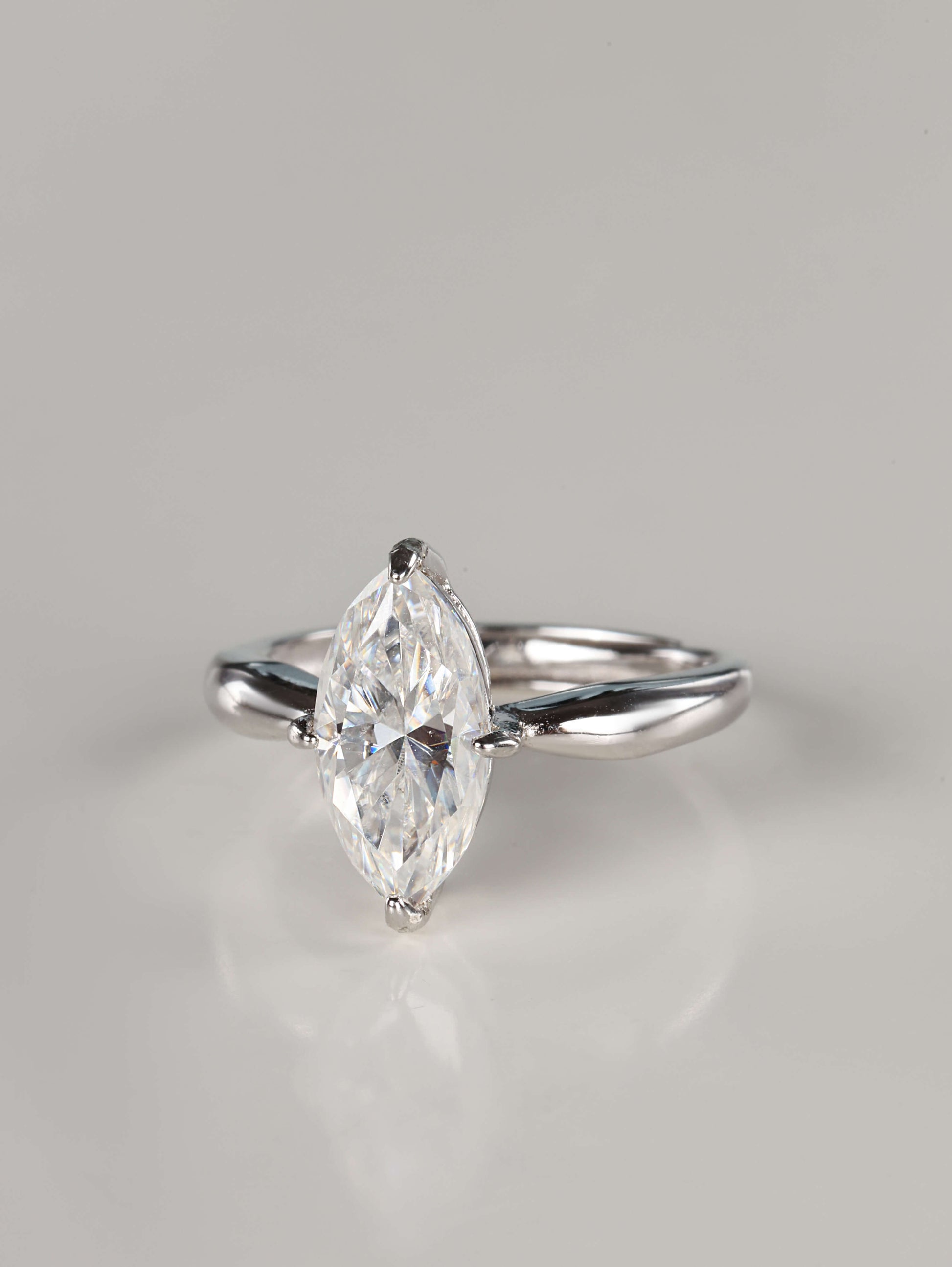 A direct front view of a 2ct moissanite marquise ring. The image emphasizes the unique 'boat' shape of the marquise stone and the protective V-shaped claw settings on the delicate pointed tips. It features a sleek, plain polished silver band that tapers toward the centre gem.
