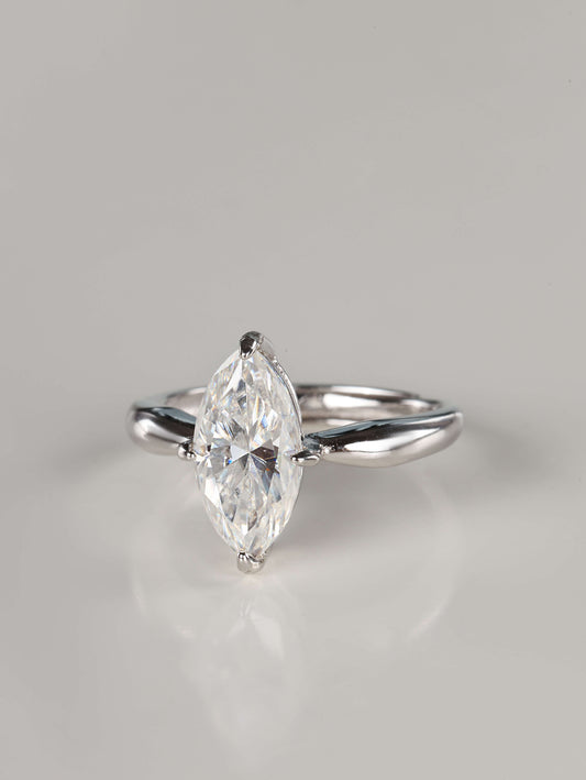 A direct front view of a 2ct moissanite marquise ring. The image emphasizes the unique 'boat' shape of the marquise stone and the protective V-shaped claw settings on the delicate pointed tips. It features a sleek, plain polished silver band that tapers toward the centre gem.