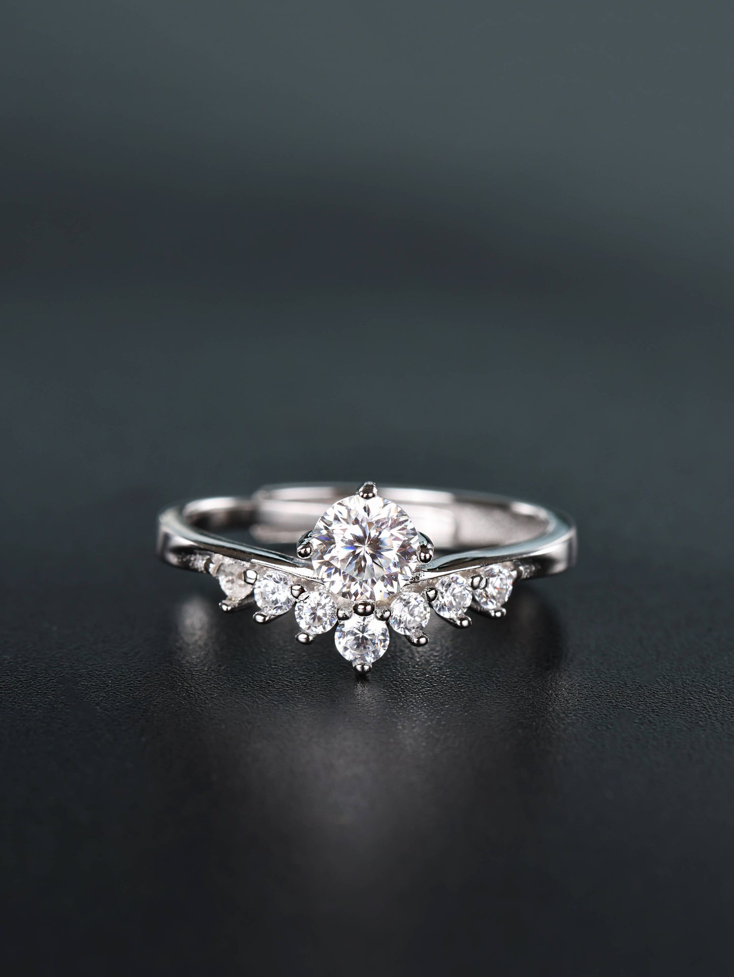 Close-up of a silver 0.5ct V-shape moissanite ring resting on a dark surface, featuring a brilliant round centre stone nestled inside a curved band with smaller pavé diamonds.