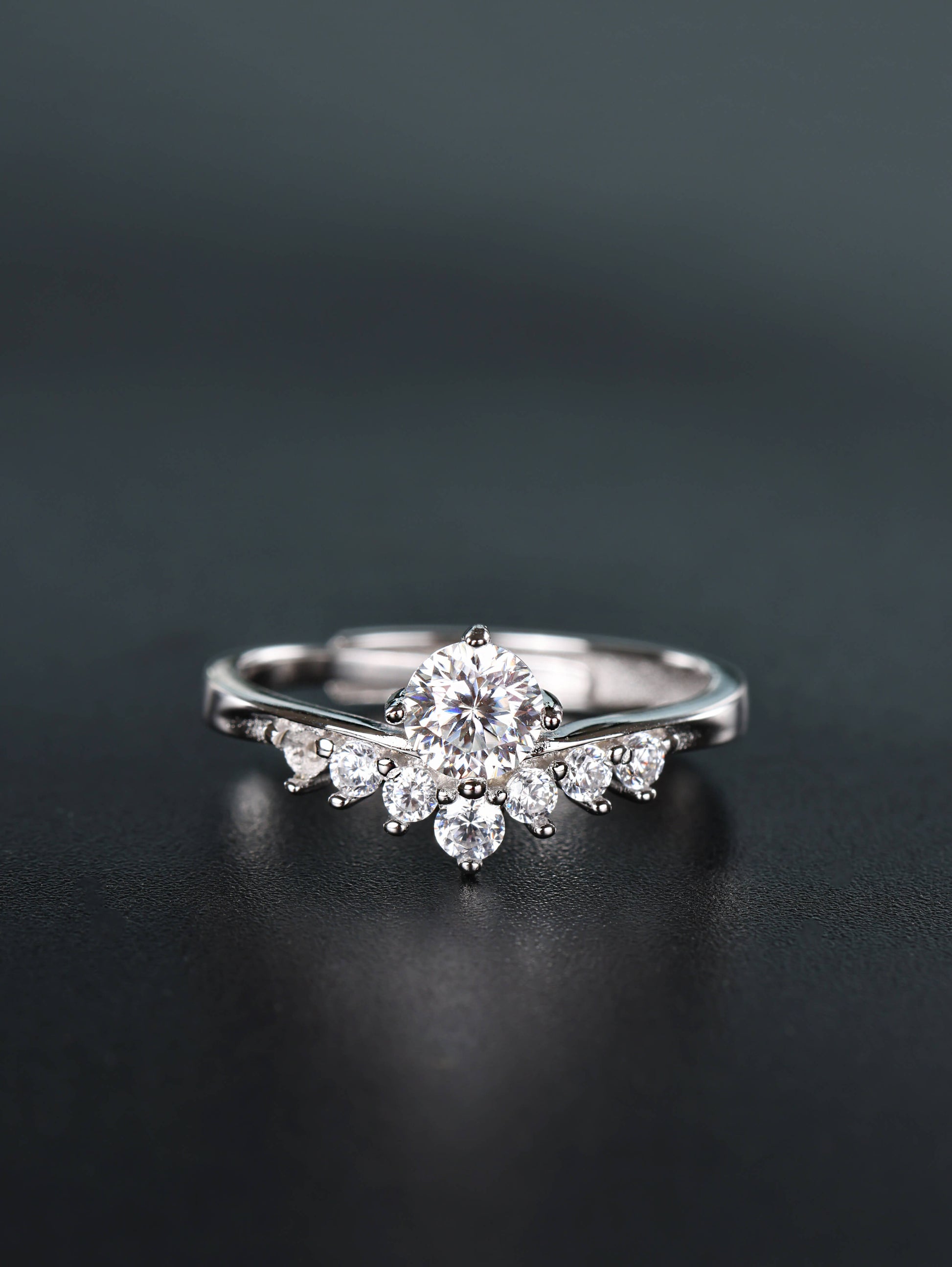 Close-up of a silver 0.5ct V-shape moissanite ring resting on a dark surface, featuring a brilliant round centre stone nestled inside a curved band with smaller pavé diamonds.