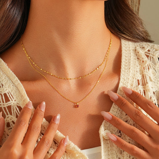 Woman wearing double layer 14K gold plated necklace with small ruby pendant.