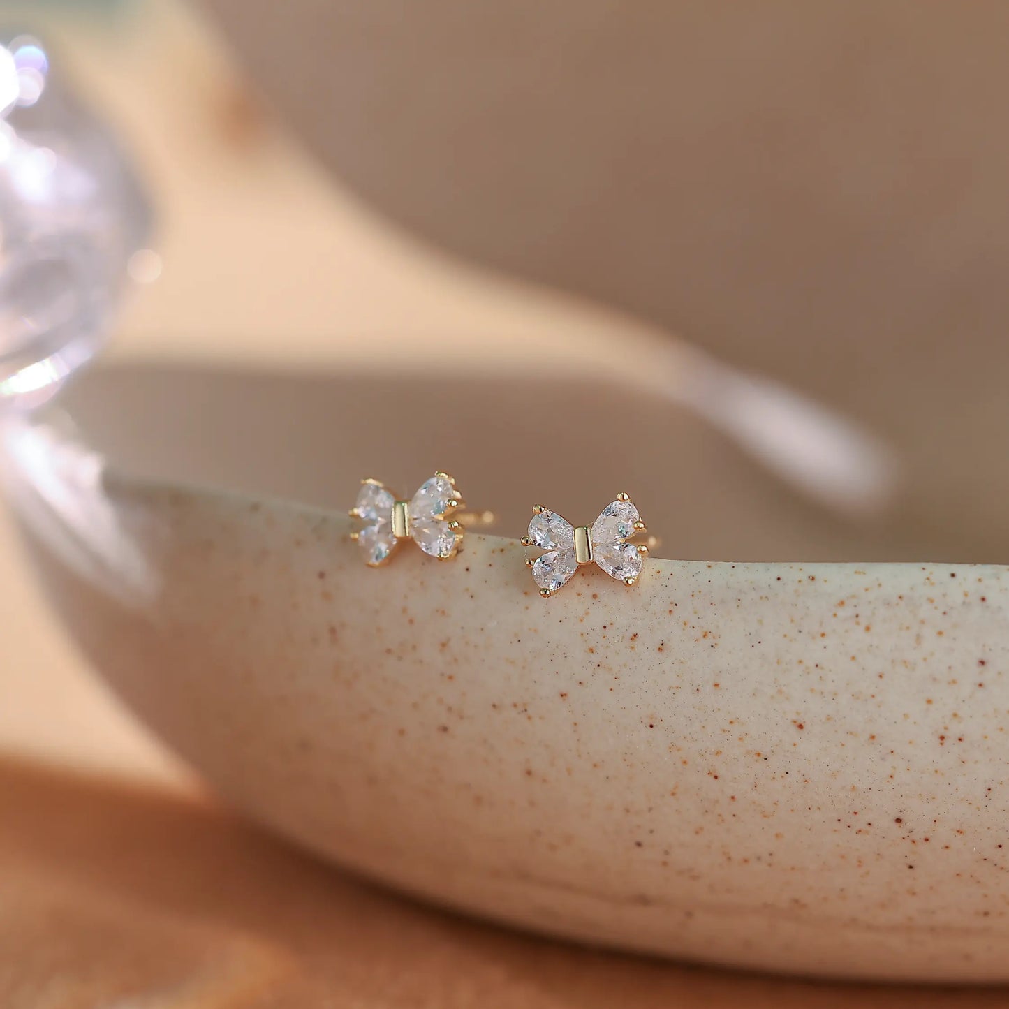 14k gold vermeil bow shaped stud earrings with pavé diamonds on a soft beige background.