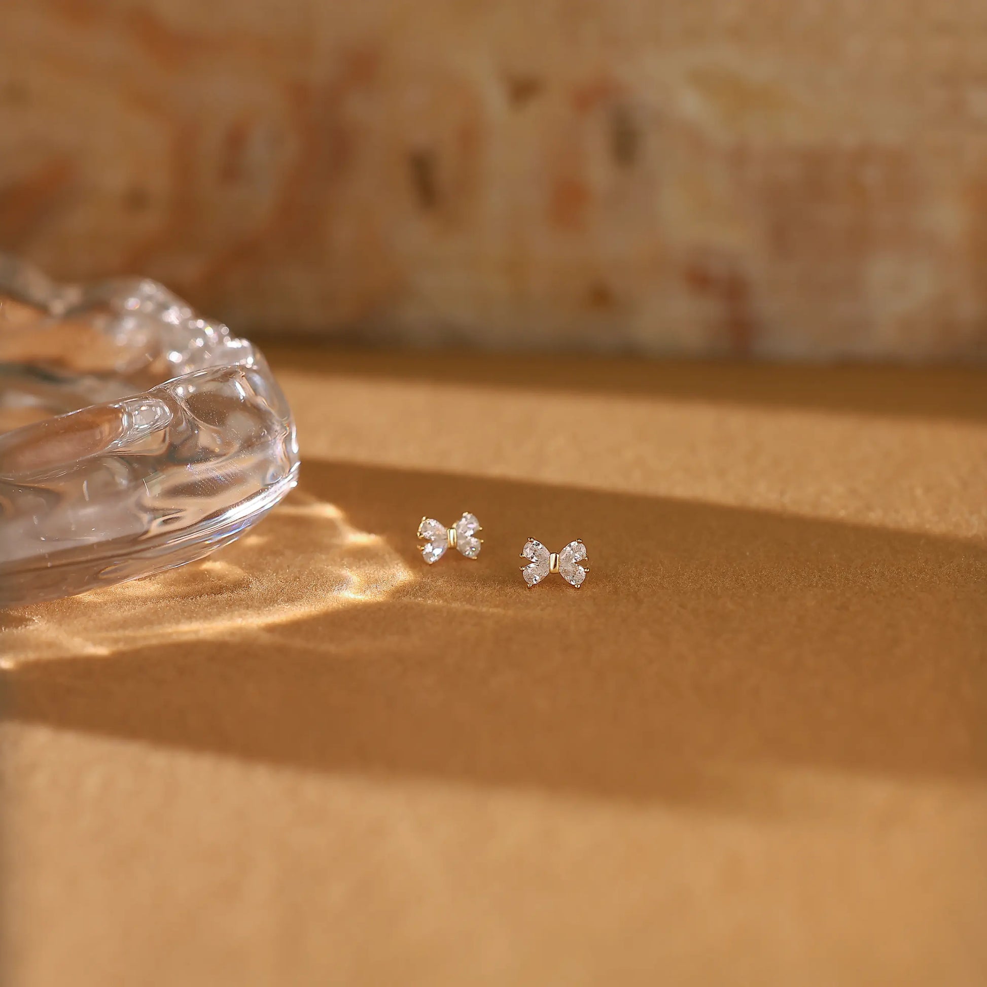 Angled close-up of delicate gold ribbon bow earrings showing the sparkling pavé stones.