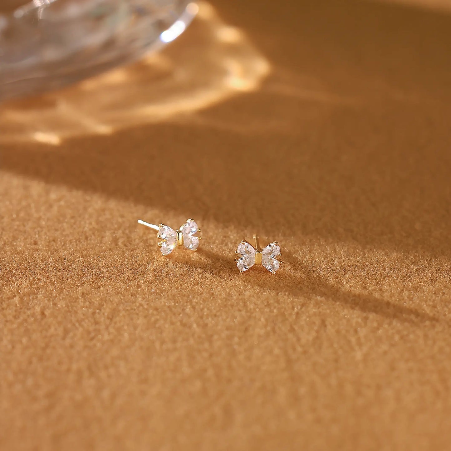 Gold bow diamond earrings resting gracefully on a cream Dialuxé suede jewelry travel pouch.