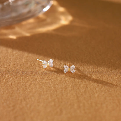 Gold bow diamond earrings resting gracefully on a cream Dialuxé suede jewelry travel pouch.