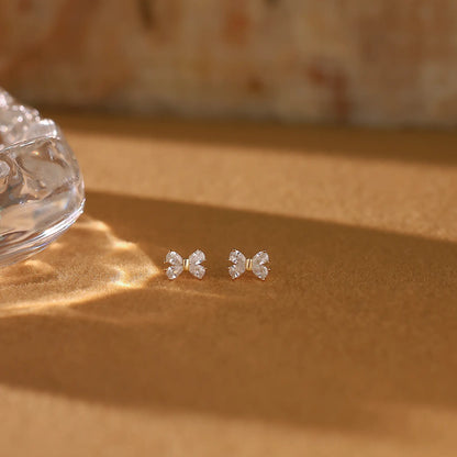 Elegant gold bow studs placed on soft linen fabric, representing quiet luxury everyday jewelry.