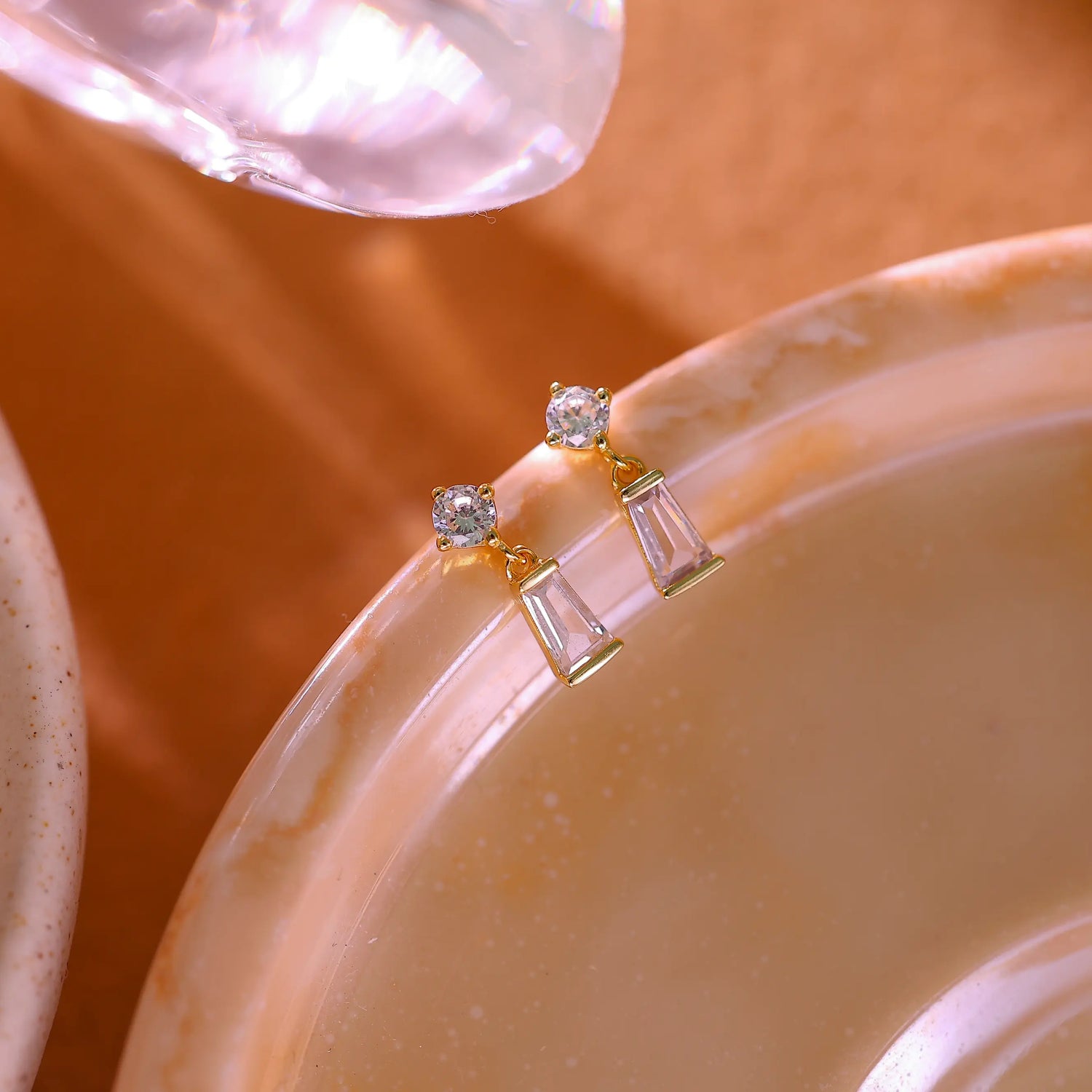 Pair of 14K gold plated sterling silver stud earrings featuring a round and baguette diamond drop.