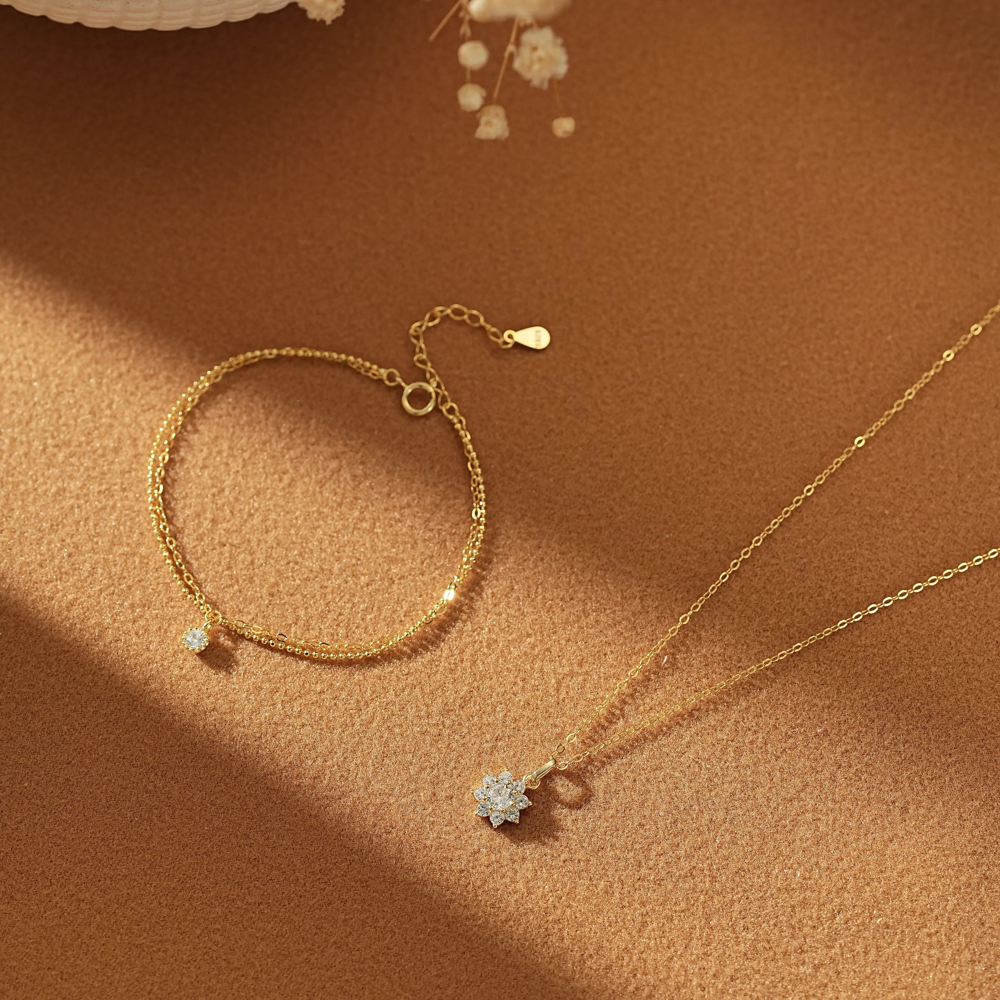 Minimalist gold jewellery set arranged together. The pairing features a sparkling snowflake motif and a timeless layered chain bracelet, designed in London.