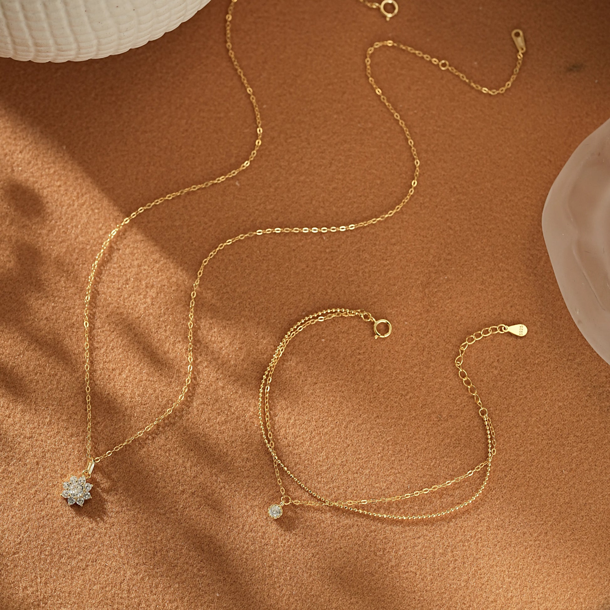 Flatlay of the Winter Glow Gift Set on beige linen. A dainty gold vermeil snowflake charm necklace placed next to a shimmering double-strand gold bracelet.