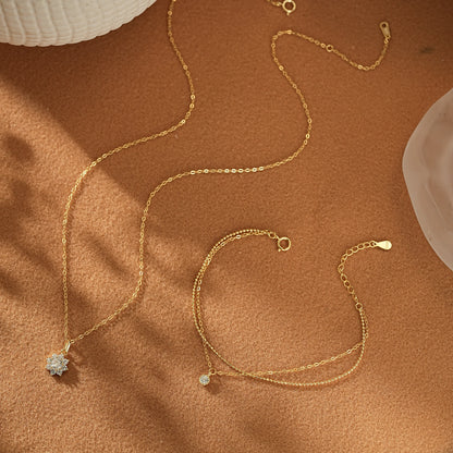 Flatlay of the Winter Glow Gift Set on beige linen. A dainty gold vermeil snowflake charm necklace placed next to a shimmering double-strand gold bracelet.